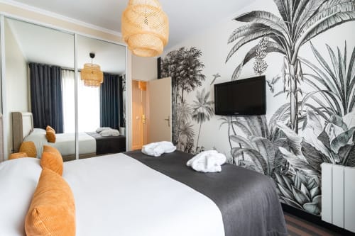 Modern bedroom in Hotel Residence Europe & Spa, Clichy, with botanical wallpaper, flat-screen TV, and mirrored wardrobe.