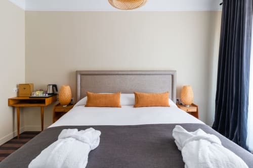 Modern bedroom in Hotel Residence Europe & Spa, Clichy, with King bed, orange pillows, wooden nightstands, and dark curtains