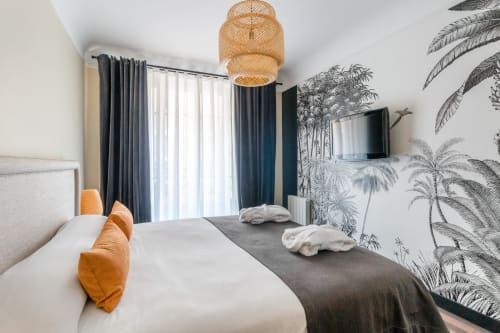 Modern 4-person apartment bedroom at Hotel Residence Europe & Spa in Clichy with king bed, tropical wallpaper, and city views