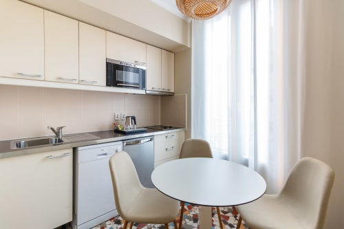 Modern kitchen and dining area in Clichy apartment with white cabinetry, stainless steel appliances, and round table with