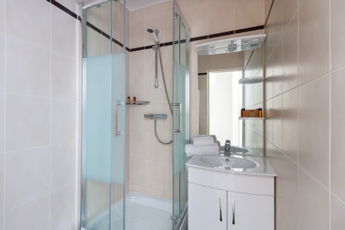 Modern bathroom in Hotel Residence Europe & Spa apartment with glass shower enclosure, white vanity sink, and beige tile
