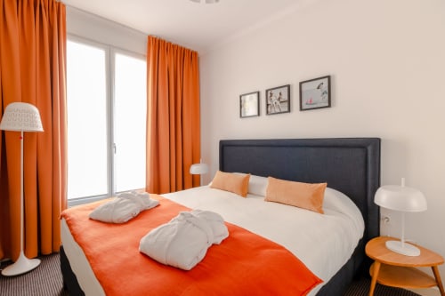 Modern hotel bedroom at Residence Europe & Spa with orange curtains, black headboard, and orange accents