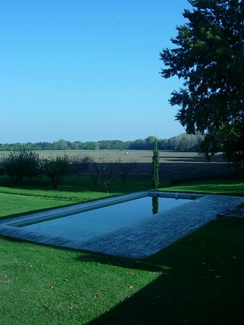 Modern rectangular pool reflecting cypress trees overlooking countryside fields at Domaine de Lamartine