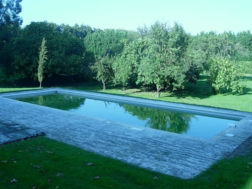 Rectangular reflecting pool with stone patio overlooking lush green trees and gardens at Domaine de Lamartine,