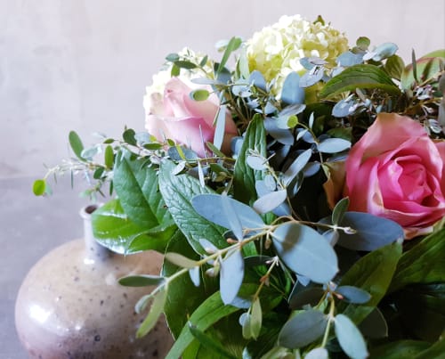 Elegant bloemstuk met roze rozen, witte hortensia's en blauwe eucalyptus in een gestructureerde vaas bij Moulin Renaudiots,