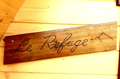 Wooden sign reading 'Le Refuge' mounted on pine wall at Belloréade glamping refuge in Belloc, France