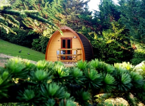 Wooden glamping pod at Belloréade in Belloc with furnished balcony surrounded by lush garden and evergreen trees.
