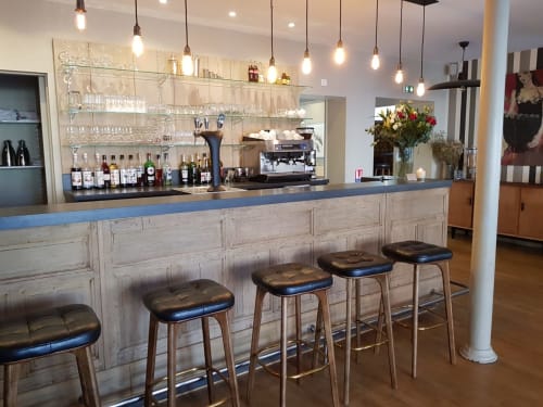 Bar moderne de l'hôtel Les Cabines à Houlgate avec tabourets en bois, suspensions luminaires et étagères de spiritueux.