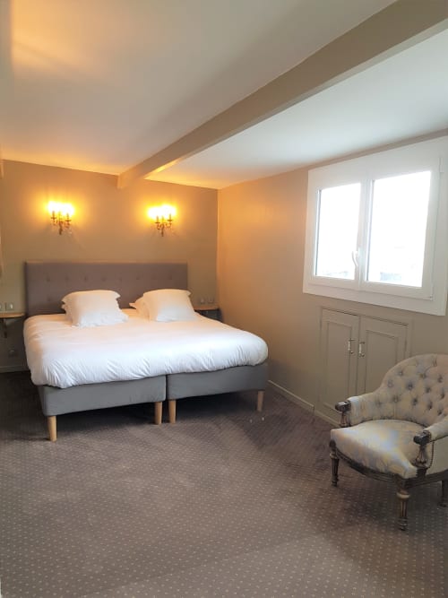 Suite spacieuse avec vue mer à l'hôtel Les Cabines à Houlgate, lit moderne, fauteuil et éclairage élégant