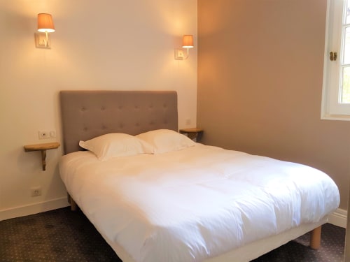Chambre moderne à l'hôtel Les Cabines à Houlgate avec lit queen-size, tête de lit taupe, appliques murales et design minimaliste