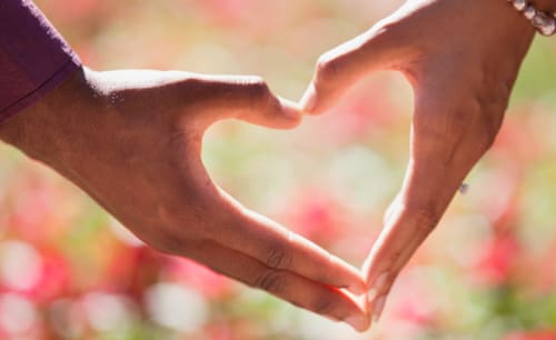 Two hands forming a heart shape with blurred flowers at Hotel Residence Europe & Spa in Clichy