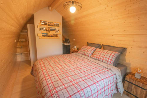 Cozy wooden glamping refuge bedroom at Belloréade with plaid bedding, heating, and garden views