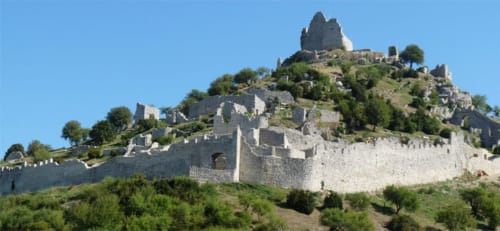 Ruines de forteresse médiévale perchées sur une colline près de Chanos-Curson, France, entourées de verdure et de ciel bleu clair