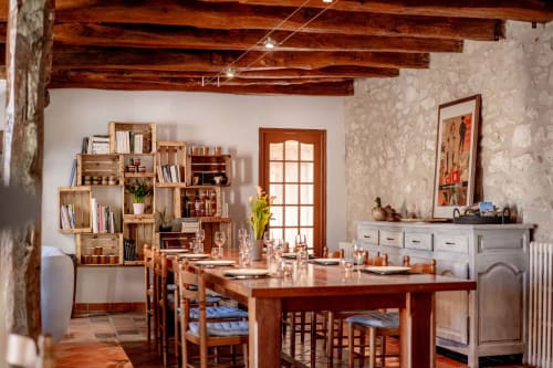Rustic gîte dining area at Le Pignié with wooden beams, dining table, open shelving, and garden view door in