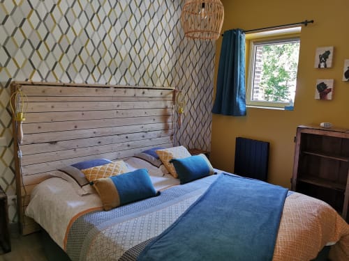 Chambre douillette à La Cour d'Hortense : lit en bois, accents bleu et orange, papier peint à motifs, vue sur le jardin
