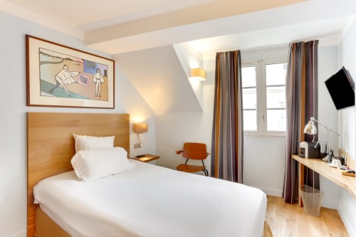 Chambre moderne à l'Hôtel Louvre Richelieu Paris avec lit en bois, rideaux rayés, bureau de travail et télévision murale