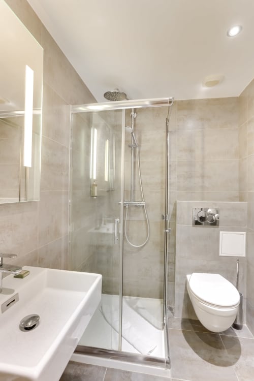 Salle de bains moderne à l'Hôtel Louvre Richelieu Paris avec douche vitrée, lavabo blanc, toilettes murales et radiateur