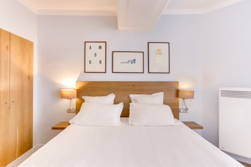 Chambre d'hôtel moderne à l'Hôtel Louvre Richelieu Paris avec tête de lit en bois, linge blanc et art mural minimaliste