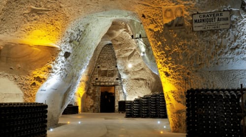 Cave historique du château d'Hermonville avec voûtes en pierre et bouteilles empilées
