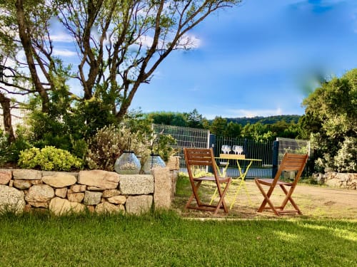 Espace de détente extérieur aux Villas Marincelu avec chaises en bois, mur de pierre et vue panoramique sur la colline de Serra di Ferro