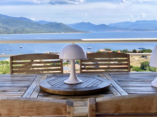 Coastal terrace at Villas Marincelu with white mushroom lamp, wooden railings overlooking Porto Pollo bay and mountains.