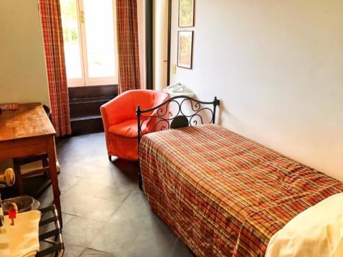 Gemütliches Einzelzimmer im Hotel Beau Rivage in Alassio mit gestreifter Bettwäsche, rotem Sessel und Türen mit Stadtblick