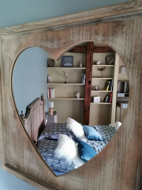 Miroir en forme de cœur reflétant une chambre douillette avec étagères, livres et objets de décoration à La Cour d'Hortense B&B en France
