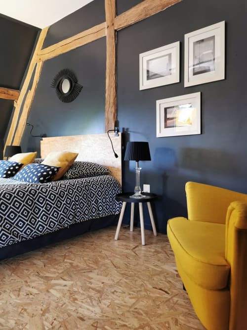 Chambre moderne à La Cour d'Hortense à Sailly-Flibeaucourt avec murs bleu foncé, lit à baldaquin en bois, fauteuil jaune