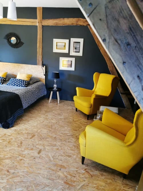 Chambre moderne à La Cour d'Hortense avec mur d'accent foncé, poutres en bois, fauteuils jaunes et linge de lit à motifs