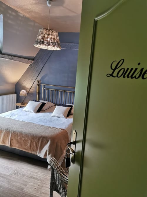 Chambre Chez Louise à La Cour d'Hortense : lit avec coussins décoratifs, luminaire suspendu en osier, mur d'accent bleu