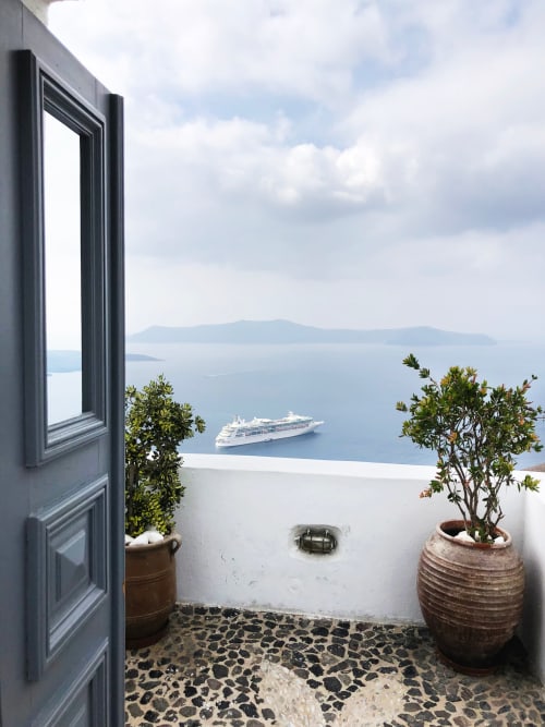 Puerta azul abierta con vista a la caldera de Santorini, crucero, macetas de terraza y mar Egeo