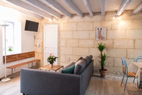 Séjour moderne du gîte Les gîtes des châteaux avec canapé gris, murs en pierre apparente, poutres en bois et télévision