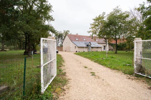 Entrée du gîte avec portail blanc et allée bordée d'arbres aux Gîtes des Châteaux à Vallières-les-Grandes, France