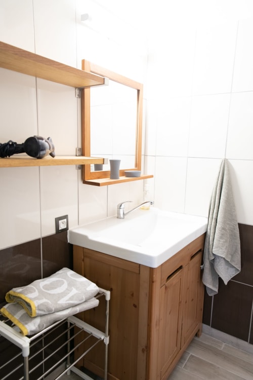 Salle de bain moderne du gîte Les châteaux avec meuble en bois, lavabo blanc, miroir encadré et porte-serviettes