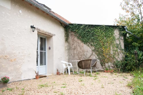 Patio de gîte aux Gîtes des Châteaux avec porte blanche, mur couvert de lierre et salon de jardin à Vallières-les-Grandes