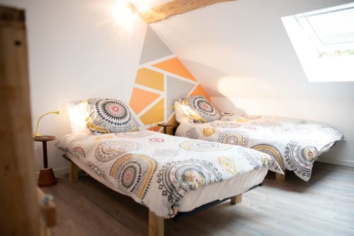 Chambre lumineuse sous les combles aux Gîtes des châteaux avec deux lits, parure géométrique colorée, poutres en bois et velux