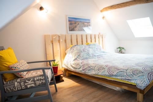 Chambre lumineuse sous les combles avec lit en bois, linge géométrique, touches jaunes et fenêtre de toit à Vallières-les-Grandes