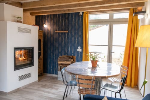Salle à manger du gîte moderne avec cheminée, mur d'accent bleu et table ronde aux Gîtes des Châteaux, Vallières-les-Grandes