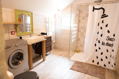 Salle de bains moderne avec douche, lavabo, machine à laver et rideau de douche aux textes français du gîte les Brûleries
