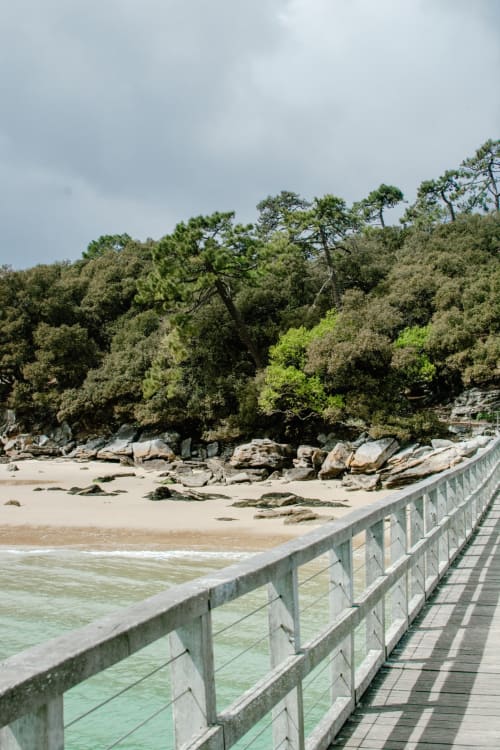 Wooden boardwalk with railing overlooking sandy beach and forested coastline at Hôtel Maison Richet, Les Sables-d'Olonne