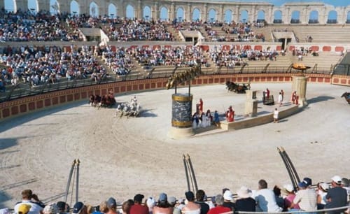 Roman amphitheater recreation with crowds in stadium seating and gladiators in sand arena