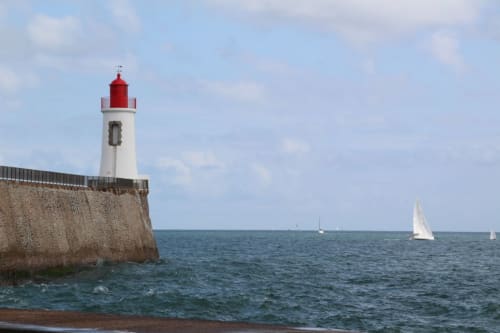 Red and white lighthouse on stone breakwater with sailboats, Les Sables-d'Olonne coastal view