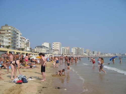 Crowded beach at Les Sables-d'Olonne with beachfront buildings, swimmers, and sandy shore on clear day