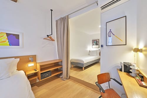 Chambre moderne de l'Hôtel Louvre Richelieu à Paris avec mobilier en bois, lit, bureau et œuvres d'art contemporain sur fond blanc