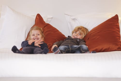 Deux enfants heureux jouant sur un lit avec des oreillers rouges à l'Hôtel Louvre Richelieu, Paris