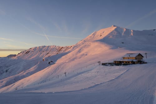 Gîte Les Boleros au coucher de soleil dans les Alpes enneigées de Queige avec pistes et remontées mécaniques