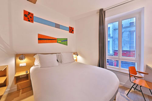 Chambre d'hôtel moderne à l'Hôtel Louvre Richelieu Paris avec lit, art mural abstrait orange et vue sur la ville