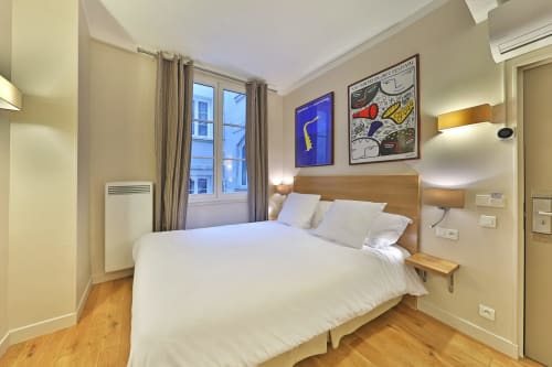 Chambre double confortable à l'Hôtel Louvre Richelieu Paris avec lit en bois, draps blancs, fenêtre, œuvres d'art et parquet