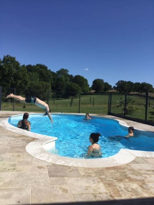 Guests enjoying a sunny day at the curved blue pool at Logis De La Bénétière in Treize-Vents, France