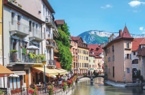 Charming old town street with colorful buildings, canal, and mountain backdrop in Annecy region